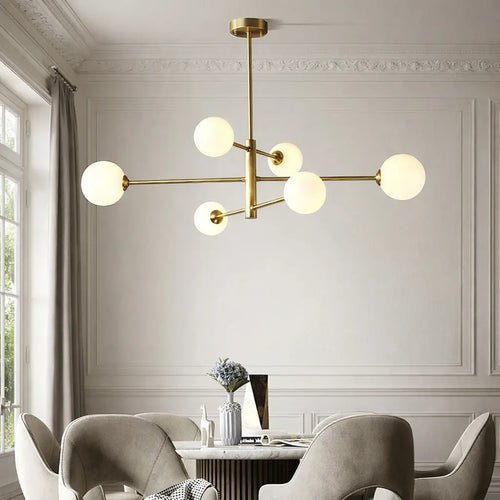 Lustre suspension moderne doré avec globes en verre opalin au-dessus d’une table à manger