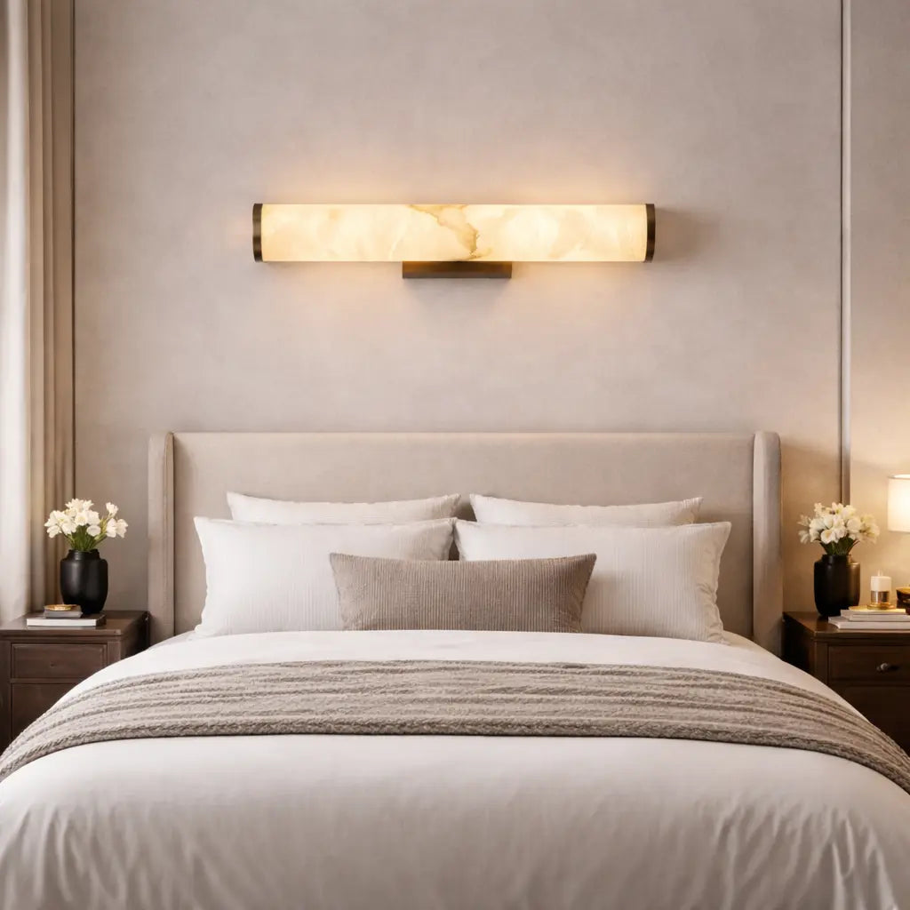 Applique murale LED cylindrique en albâtre beige effet marbre et métal bronze installée horizontalement au-dessus d’un lit